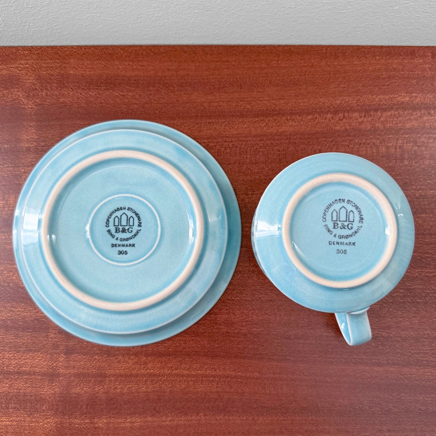 Quistgaard Cordial Palet Turquoise Tea Cup with Saucer showing the backstamp of vintage ceramic cup and matching saucer in light turquoise color on wooden surface.