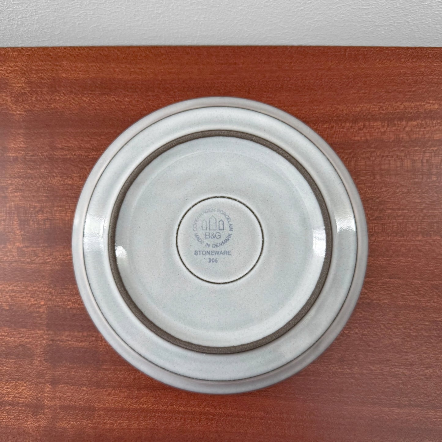 Bottom view of a ceramic saucer from the Quistgaard Cordial Tea Cup Trio Set, showing vintage stoneware markings and subtle neutral glaze on a wooden surface.