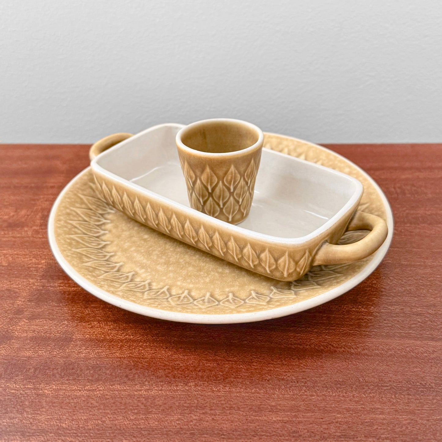 Quistgaard Relief Tableware Set with beige ceramic large cake plate, rectangular oven dish with handles, and matching egg cup featuring textured relief pattern.
