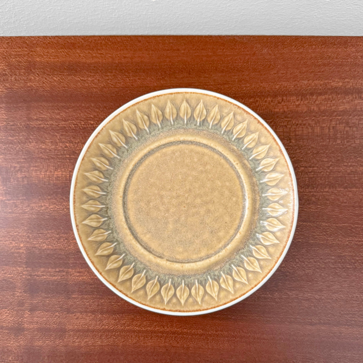 Quistgaard Relief Tea Cup Trio Set cake plate with embossed leaf pattern in muted beige and green tones on a wooden surface, showcasing vintage Scandinavian ceramics.