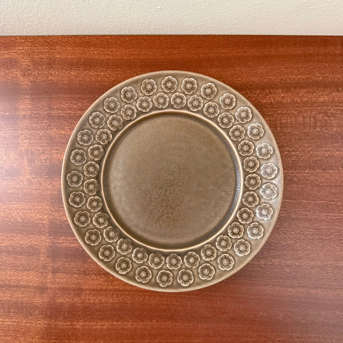 Quistgaard Umbra Tea Cup Trio Set cake plate with textured brown ceramic surface featuring a ring of embossed floral patterns on a wooden table.