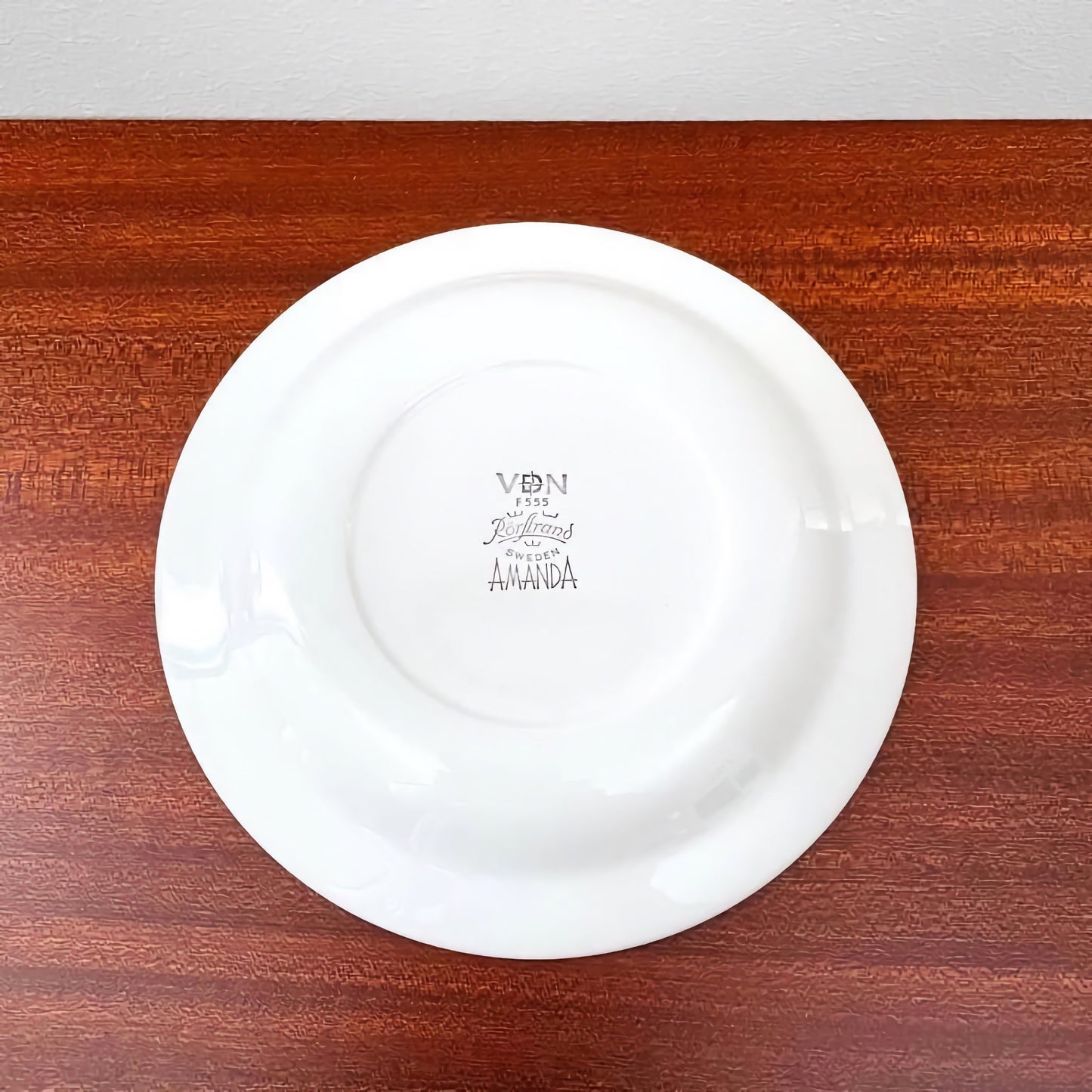 White ceramic saucer from the Rörstrand Amanda Tea Cup Trio Set showing vintage Nordic craftsmanship with the maker's mark on the underside, displayed on a wooden surface.