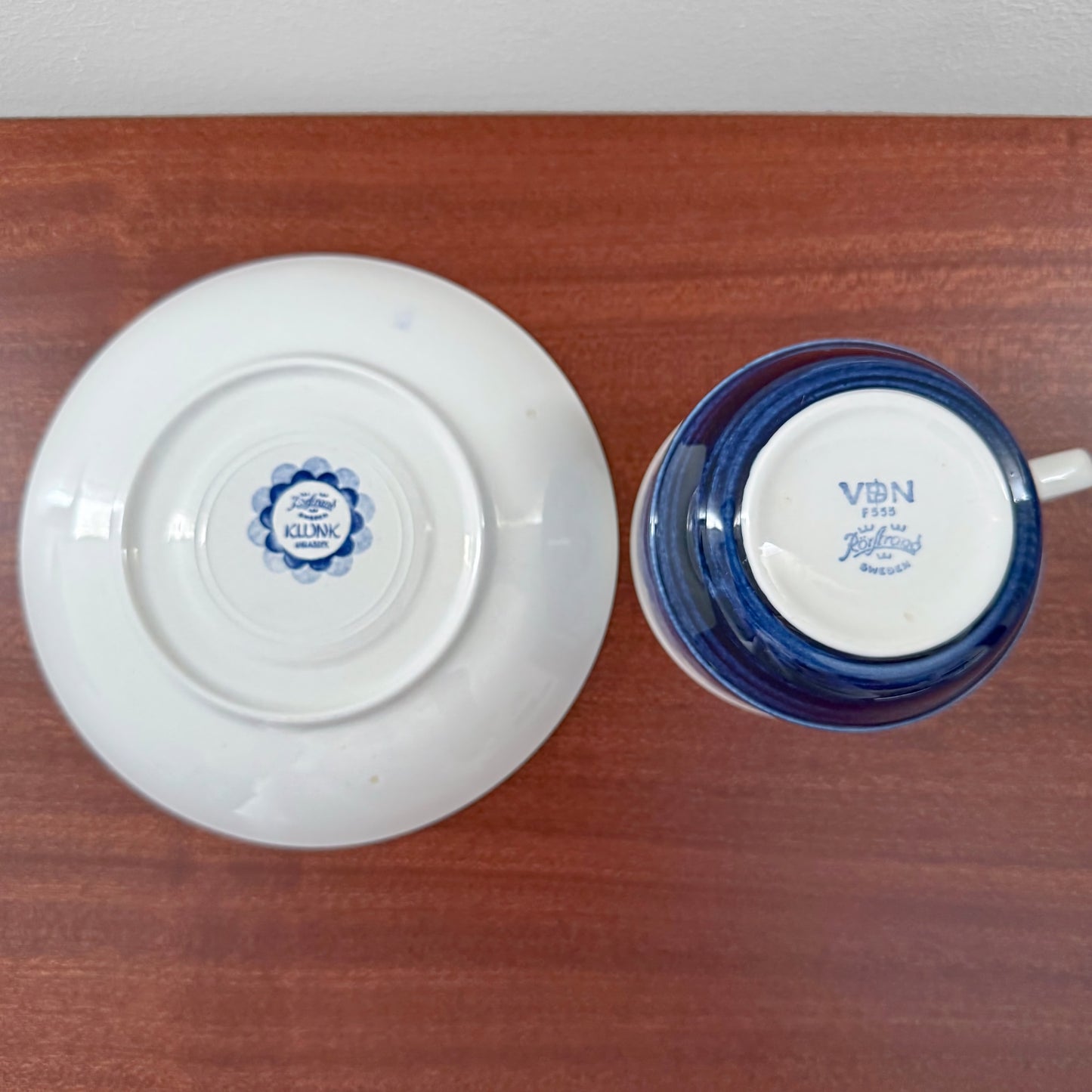 Bottom view of a vintage Rörstrand Klunk Tea Cup with Saucer showing maker’s marks and blue floral and text details on a wooden surface.