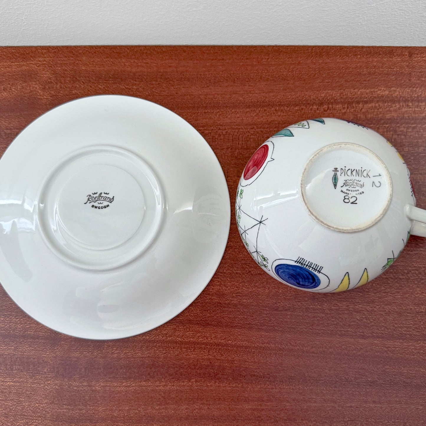 Rörstrand Picknick Tea Cup with Saucer showing the underside with vintage markings and colorful mid-century Scandinavian design details on a wooden surface.