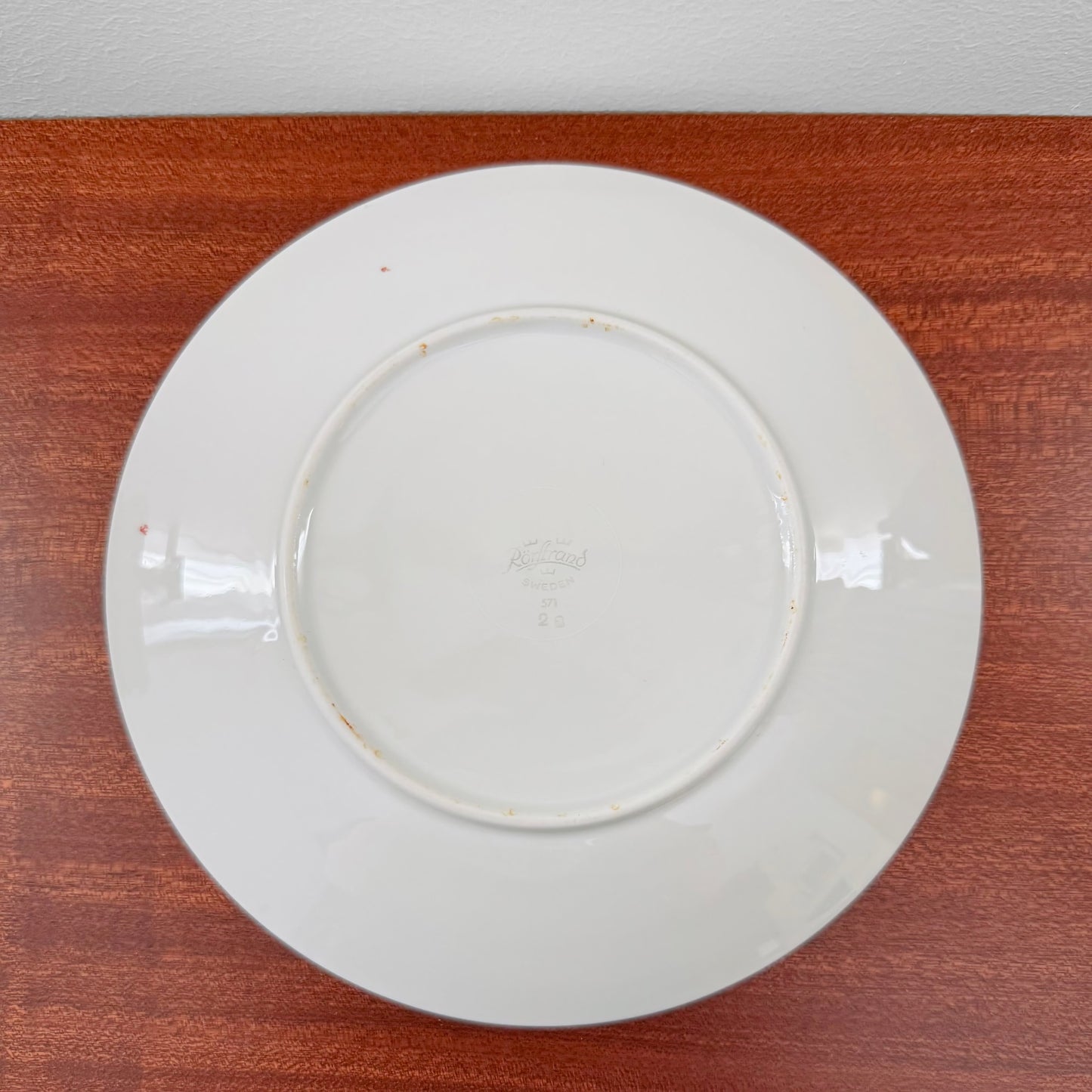 Back view of a white ceramic plate from the Rörstrand Striped Tea Cup Trio Set showing vintage markings and light signs of use on a wooden surface.