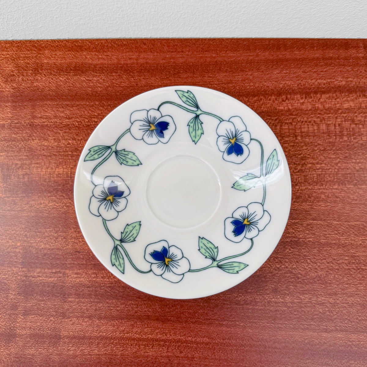 Rörstrand Sylvia Coffee Cup with Saucer featuring a vintage ceramic saucer decorated with delicate blue and white floral patterns and green leaves on a wooden surface.