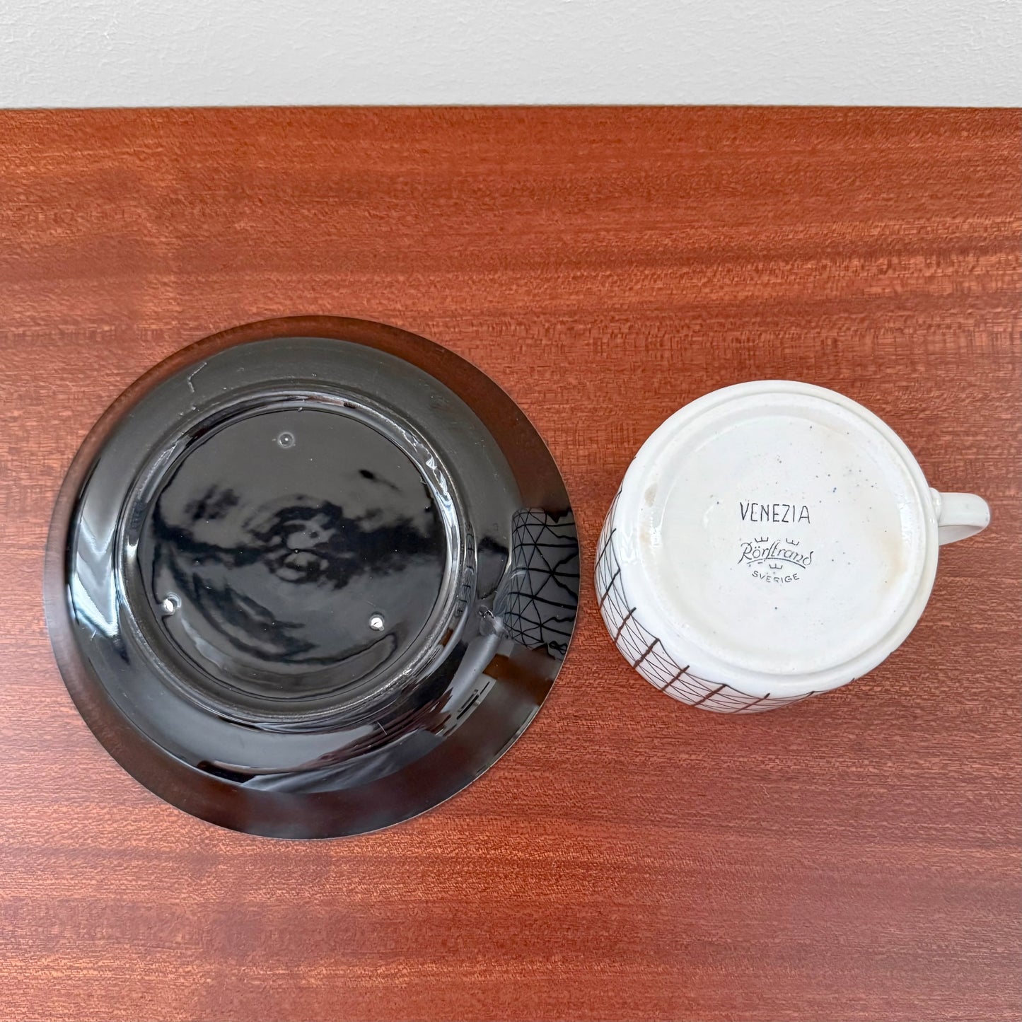 Rörstrand Venezia Coffee Cup with Saucer shown from above on a wooden surface, featuring the cup upside down displaying its vintage markings and the glossy dark saucer beside it.