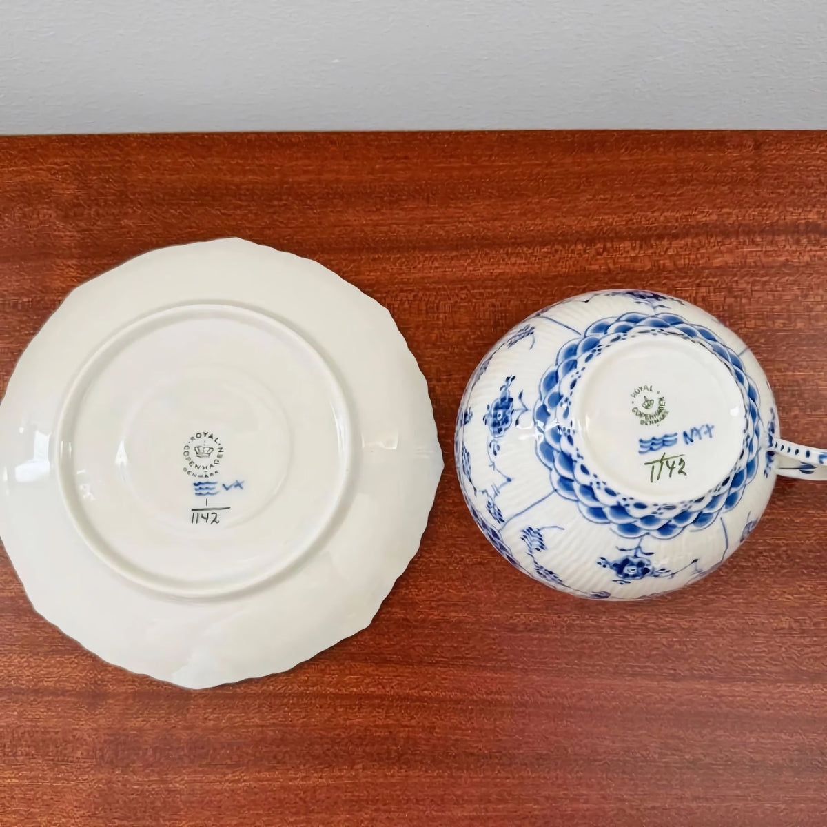 Bottom view of the Royal Copenhagen Blue Fluted Full Lace Large Tea Cup Trio Set showing the ceramic marks and intricate blue floral patterns on the cup and the saucer on a wooden surface.