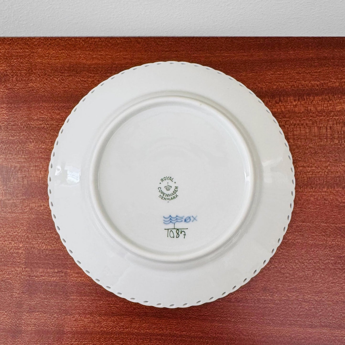 Back view of a vintage ceramic plate from the Royal Copenhagen Blue Fluted Full Lace Tea Cup Trio Set showing maker's marks and decorative scalloped edge on a wooden surface.