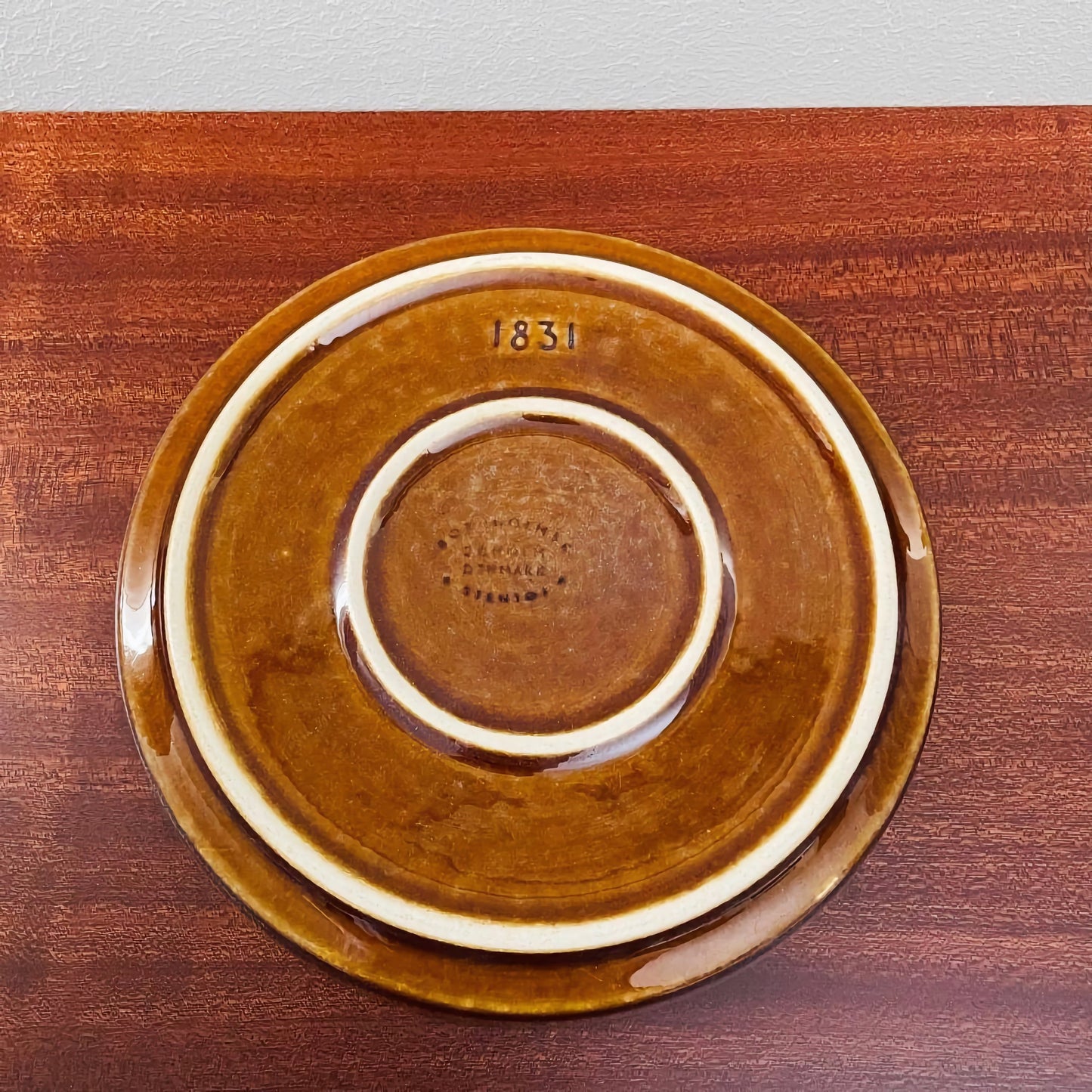 Bottom view of the cake plate from the Søholm Granit Brown Tea Cup Trio Set showing its warm brown ceramic finish and vintage markings on a wooden surface.