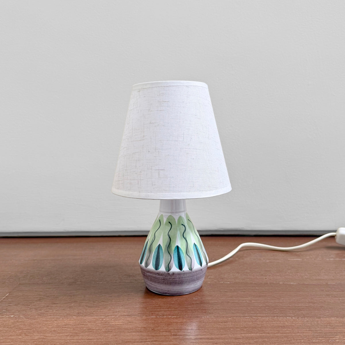 Swedish Small Botanical Table Lamp in ceramic with an abstract botanical motif and new white fabric shade on a wooden surface