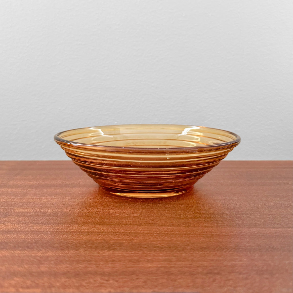 Aino Aalto Karhula Bölgeblick Amber Glass Bowl with ribbed design, showcasing vintage Scandinavian glass craftsmanship in warm amber tones on a wooden surface.