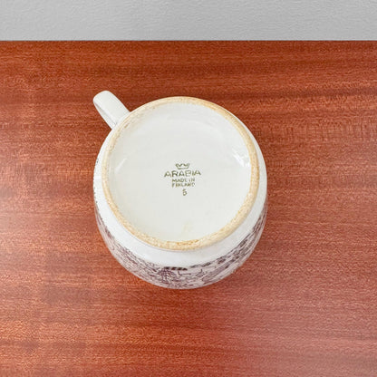 Bottom view of a vintage Arabia Finland Emilia Large Cocoa Cup with Saucer showing maker’s mark on ceramic, placed on a wooden surface, highlighting authentic Scandinavian craftsmanship.