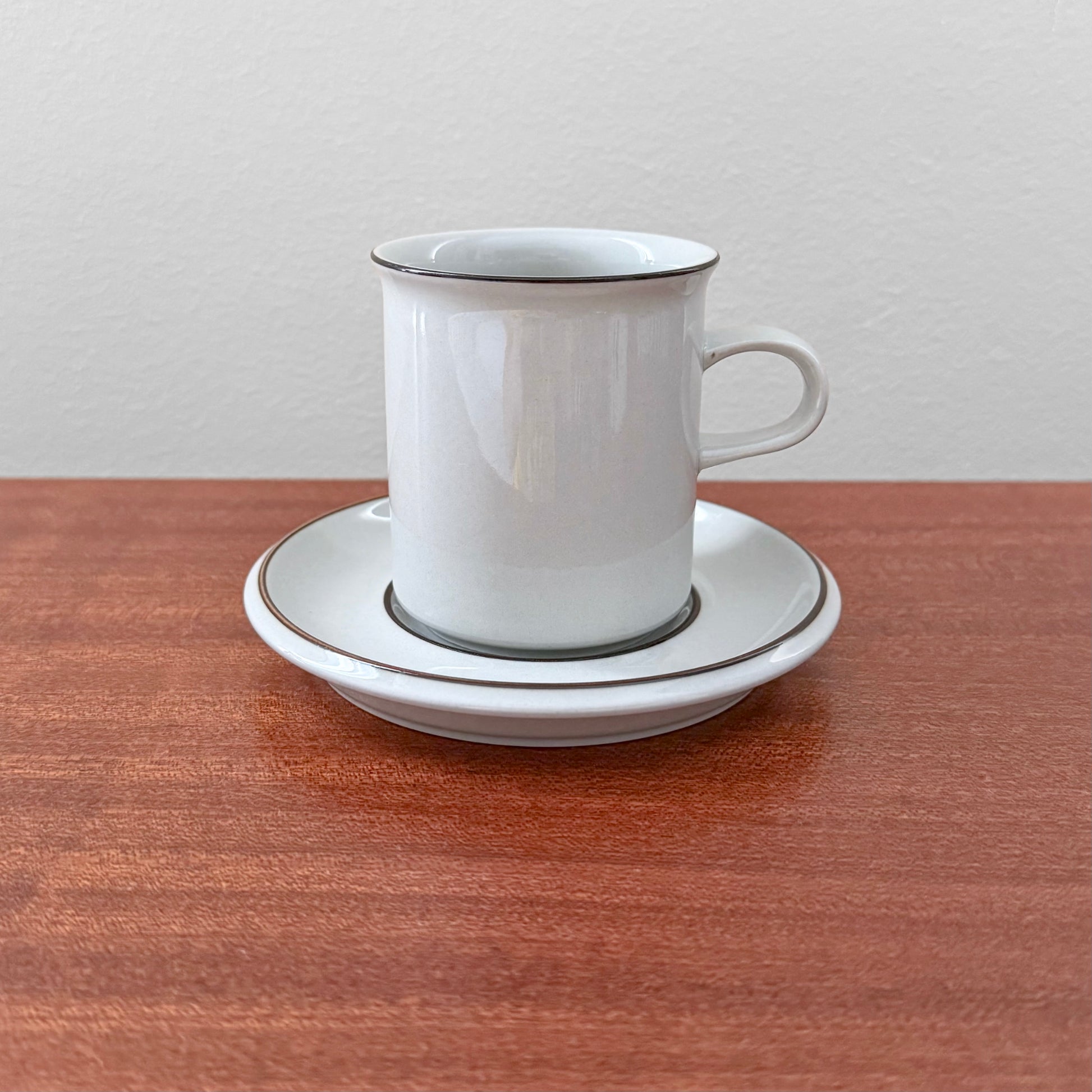 Arabia Finland Fennica Coffee Cup with Saucer featuring simple white ceramic design with thin dark trim, displayed on a wooden surface, highlighting vintage Nordic drinkware craftsmanship.