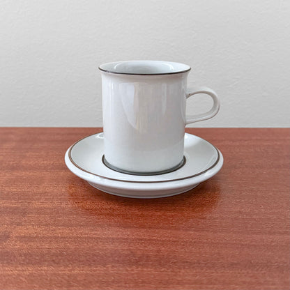 Arabia Finland Fennica Coffee Cup with Saucer featuring simple white ceramic design with thin dark trim, displayed on a wooden surface, highlighting vintage Nordic drinkware craftsmanship.