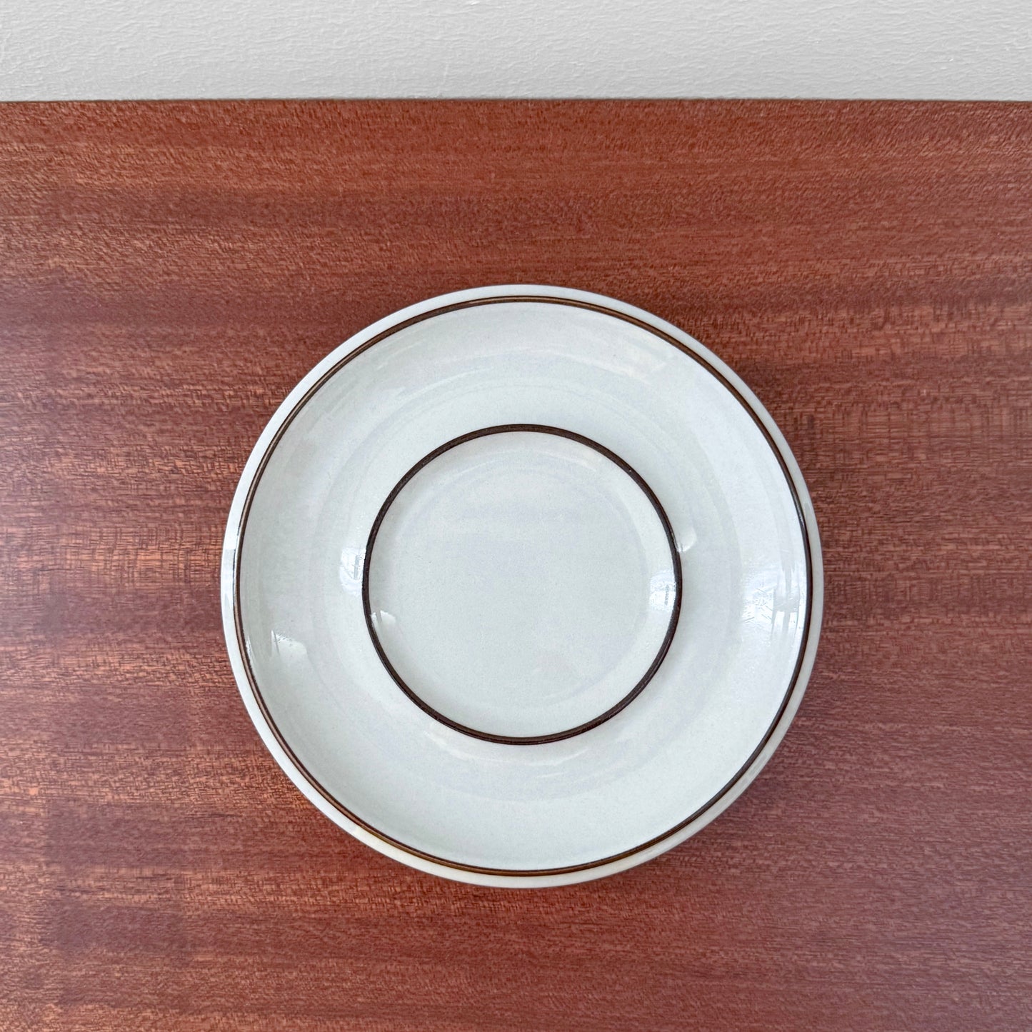 Arabia Finland Fennica Coffee Cup with Saucer showcasing a vintage white saucer with two brown concentric rings, set on a wooden surface, reflecting Nordic ceramic design.