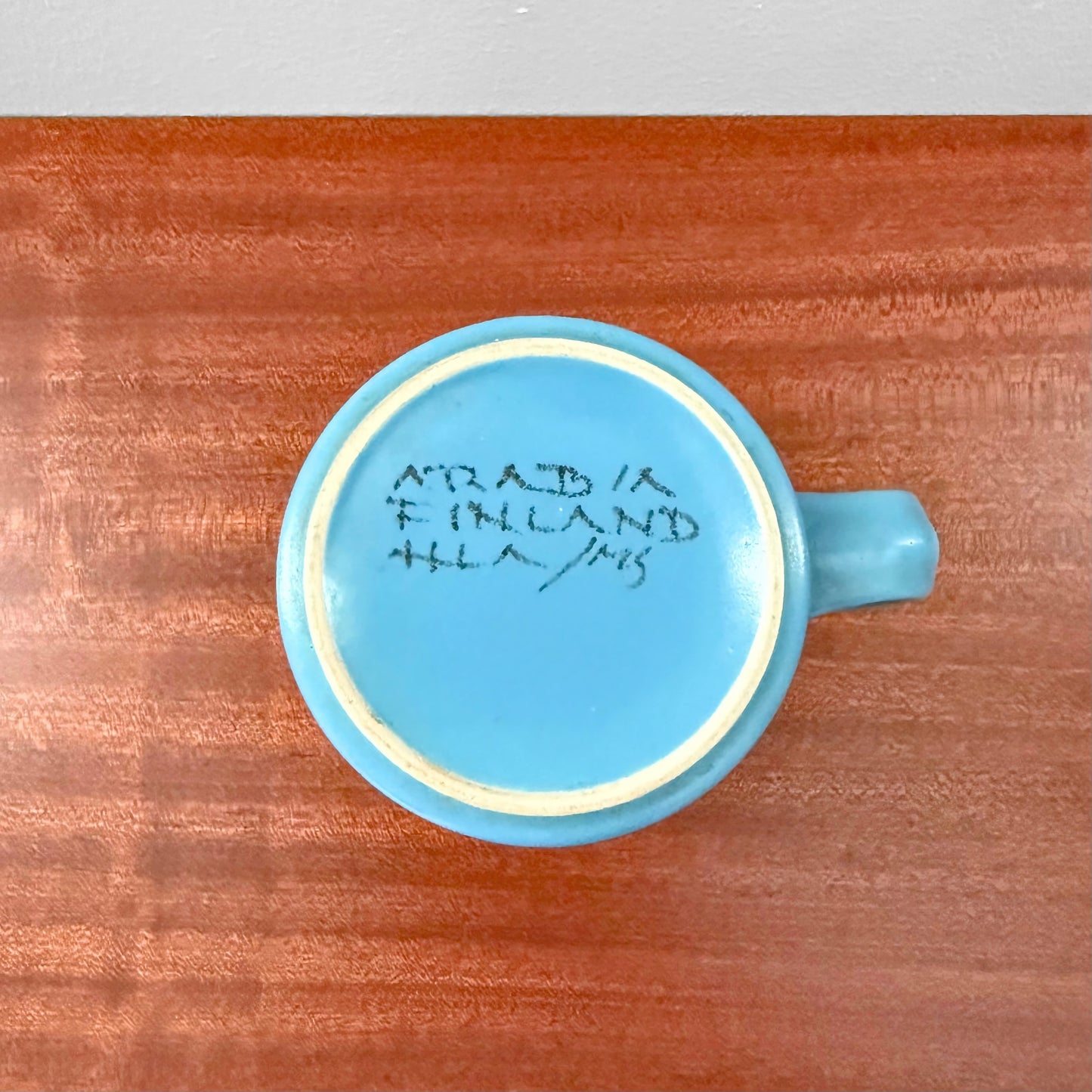 Bottom view of a vintage hand-painted Arabia Finland Hilkka-Liisa Ahola Large Blue Mug showing the signature and maker's mark on the base, placed on a wooden surface.