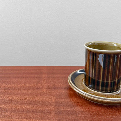 Arabia Finland Kosmos Coffee Cup with Saucer in brown and beige ceramic, vintage design with vertical stripes on the cup, displayed on a wooden surface against a plain wall.