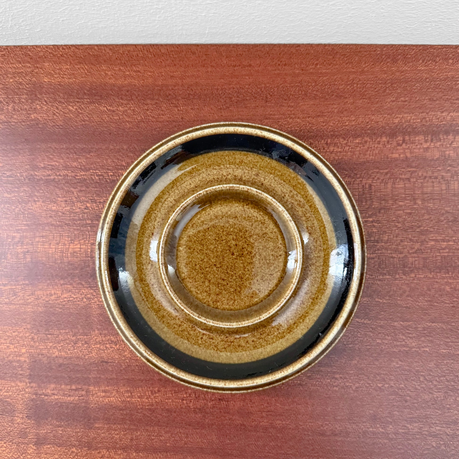Arabia Finland Kosmos Coffee Cup with Saucer showing a vintage ceramic saucer with brown and black glaze on a wooden surface, featuring Nordic craftsmanship and mid-century design.