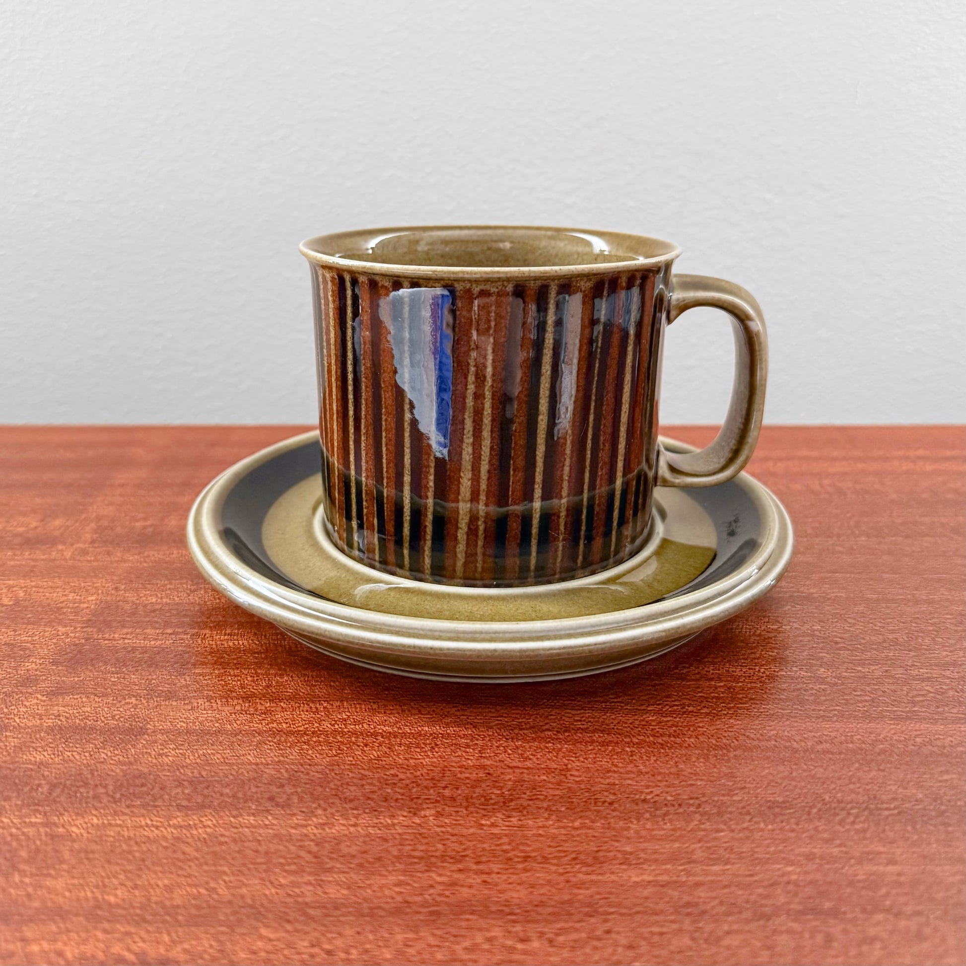 Arabia Finland Kosmos Large Mug with Saucer featuring a vintage ceramic cup with striped brown and black glaze, accompanied by a matching saucer on a wooden surface.