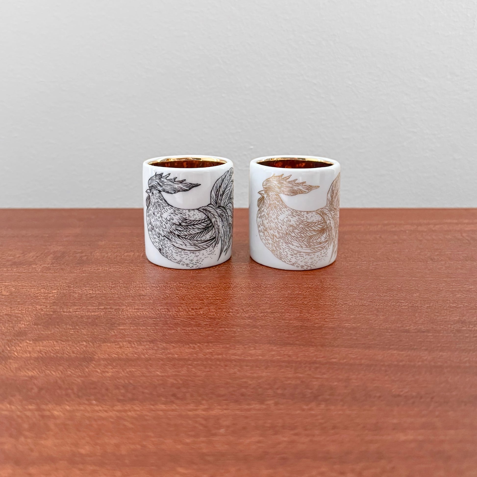 Pair of Arabia Finland Kukko Egg Cups featuring detailed hand-painted rooster designs in black and brown tones on white ceramic, showcasing vintage Scandinavian craftsmanship.