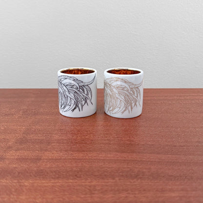 Pair of Arabia Finland Kukko Egg Cups featuring vintage hand-painted botanical designs in black and gold on white ceramic with a glossy finish, displayed on a wooden surface.