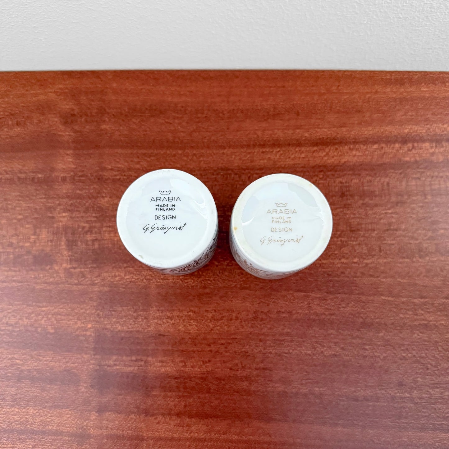 Bottom view of a pair of Arabia Finland Kukko Egg Cups showing the hand-painted signature and maker’s mark on a wooden surface.
