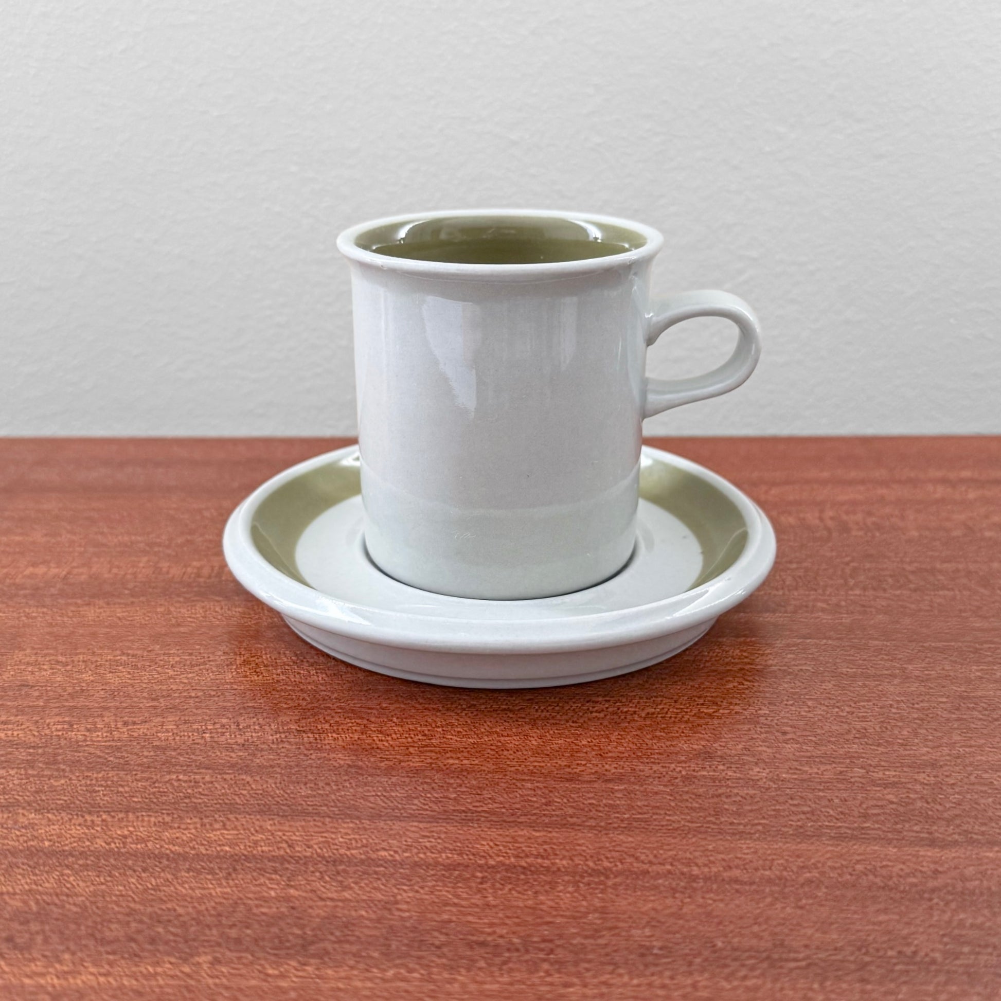 Arabia Finland Oliivi Coffee Cup with Saucer in white and olive green ceramic, vintage Nordic drinkware piece displayed on a wooden surface.