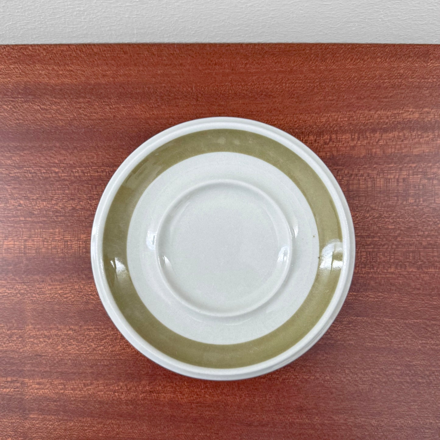 Saucer from Arabia Finland Oliivi Coffee Cup with Saucer featuring a wide olive green band on white ceramic, displayed on wooden surface in vintage Nordic design style.