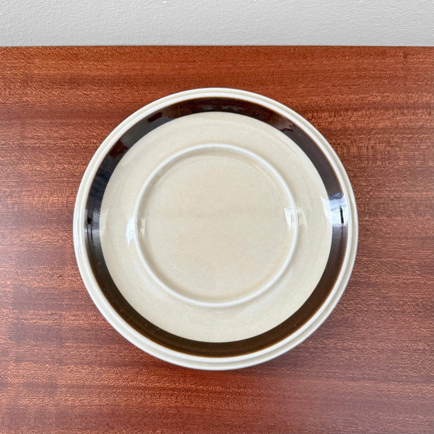 Top view of the Arabia Finland Ruija Large Mug with Saucer showing a vintage ceramic saucer with beige center and dark brown border on a wooden surface.