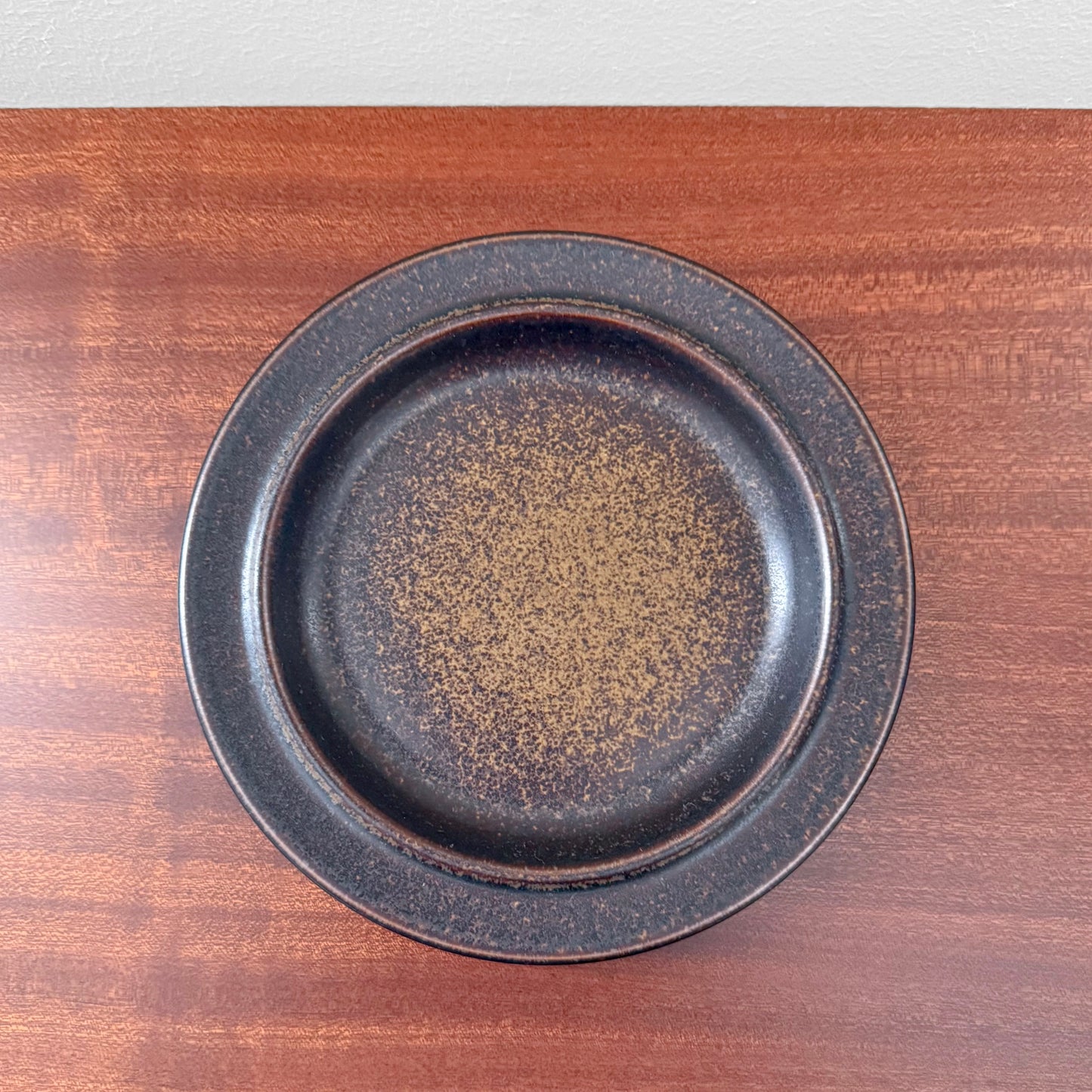Single Arabia Finland Ruska Cake Plate featuring a dark speckled glaze, showcasing vintage Nordic ceramic craftsmanship on a wooden surface.