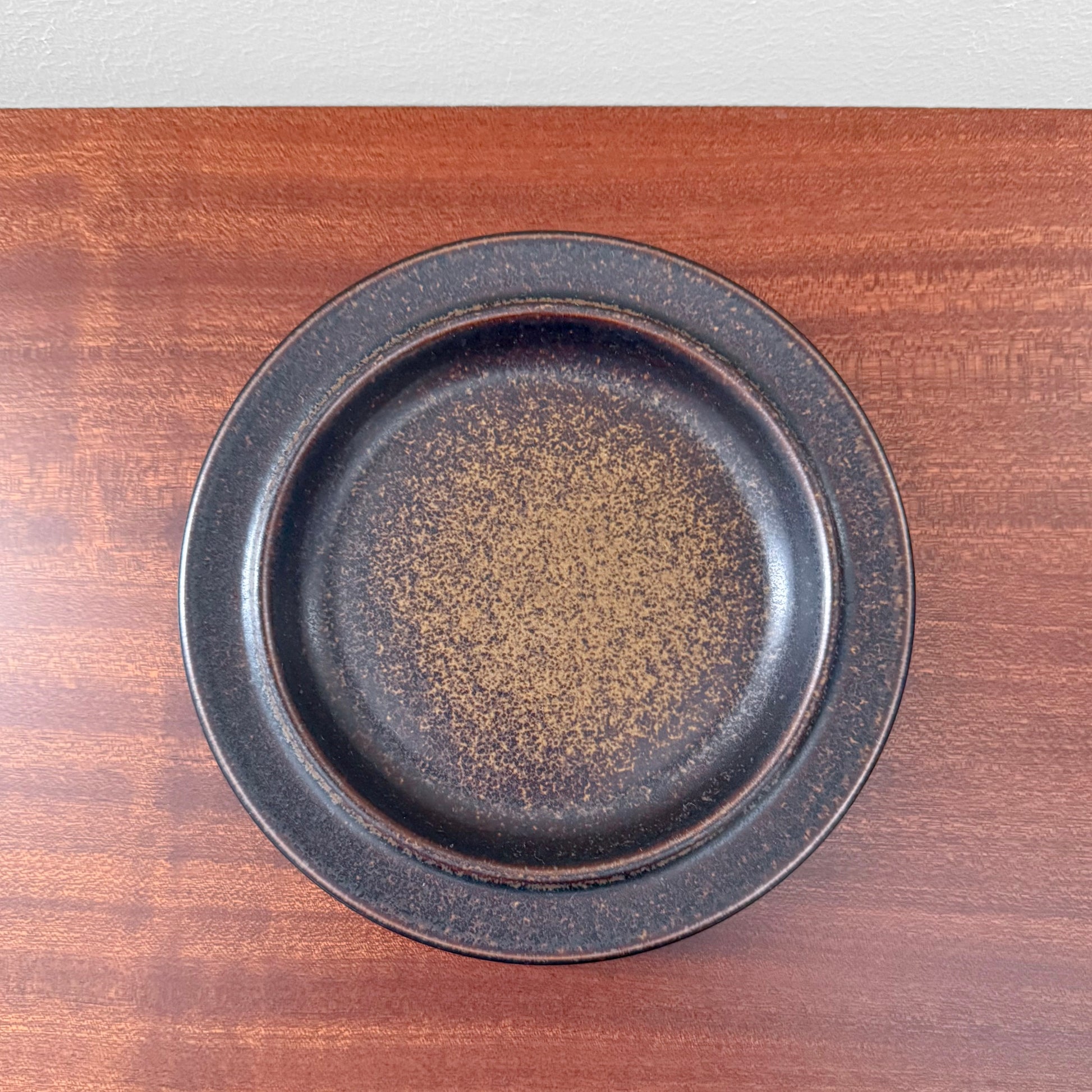 Single Arabia Finland Ruska Cake Plate featuring a dark speckled glaze, showcasing vintage Nordic ceramic craftsmanship on a wooden surface.
