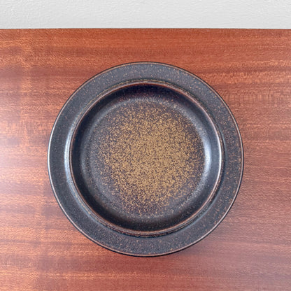Single Arabia Finland Ruska Cake Plate featuring a dark speckled glaze, showcasing vintage Nordic ceramic craftsmanship on a wooden surface.