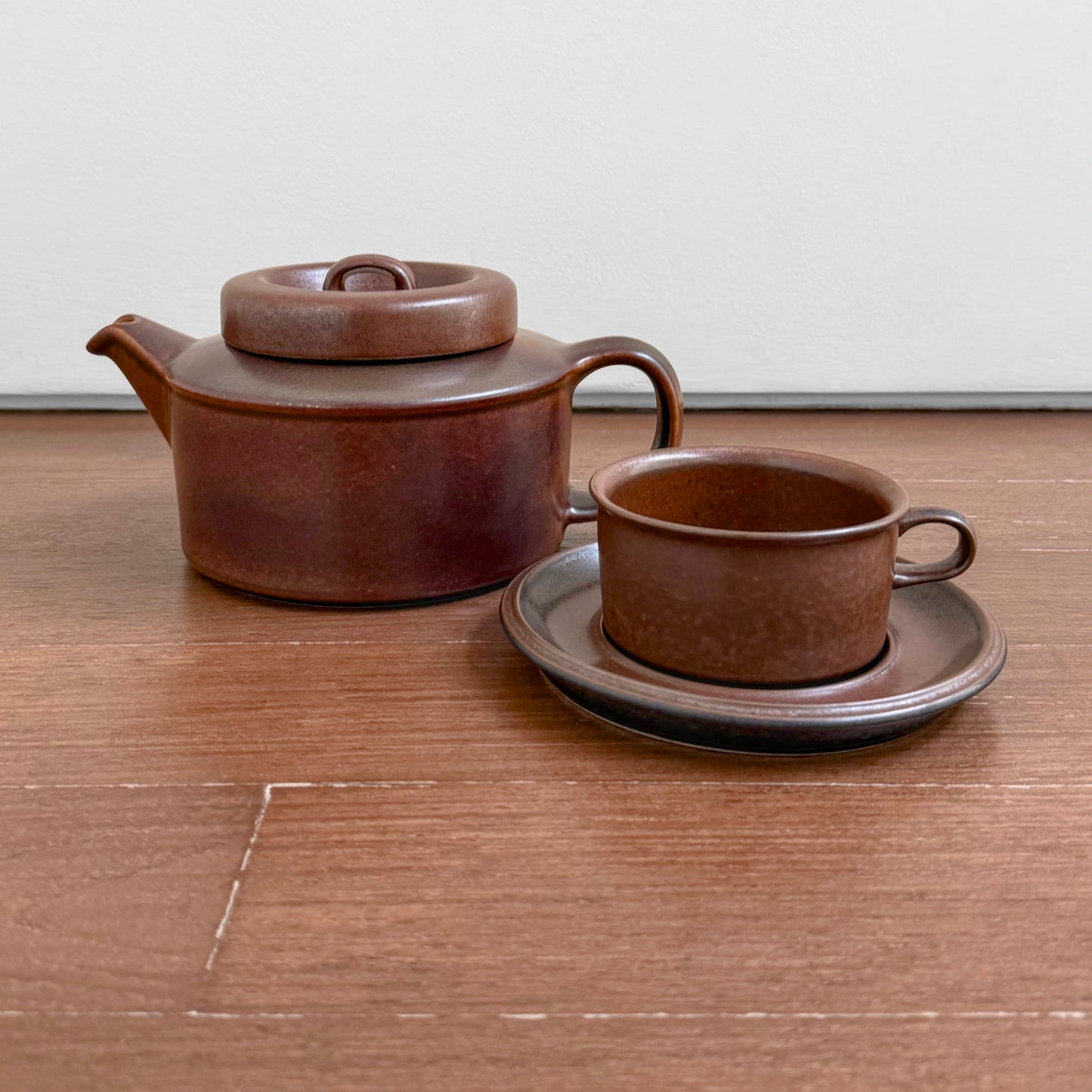 Arabia Finland Ruska Early Tea Set vintage ceramic brown teapot with lid, matching tea cup and saucer on wooden surface, showcasing Nordic drinkware craftsmanship.