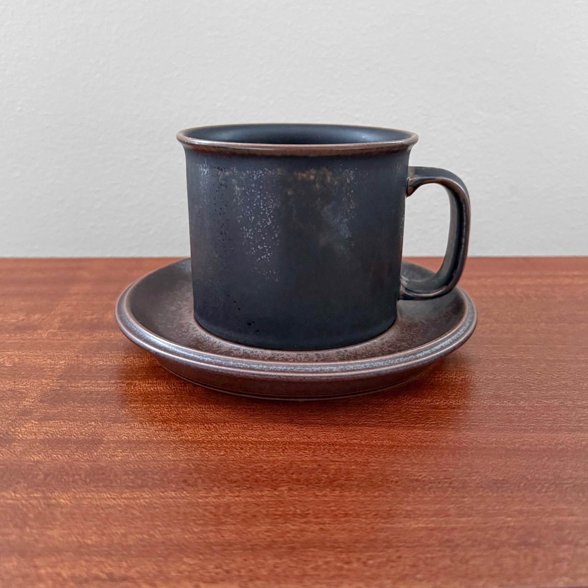 Arabia Finland Ruska Large Mug with Saucer in dark matte stoneware, showcasing vintage Nordic ceramic design on a wooden surface against a plain background.