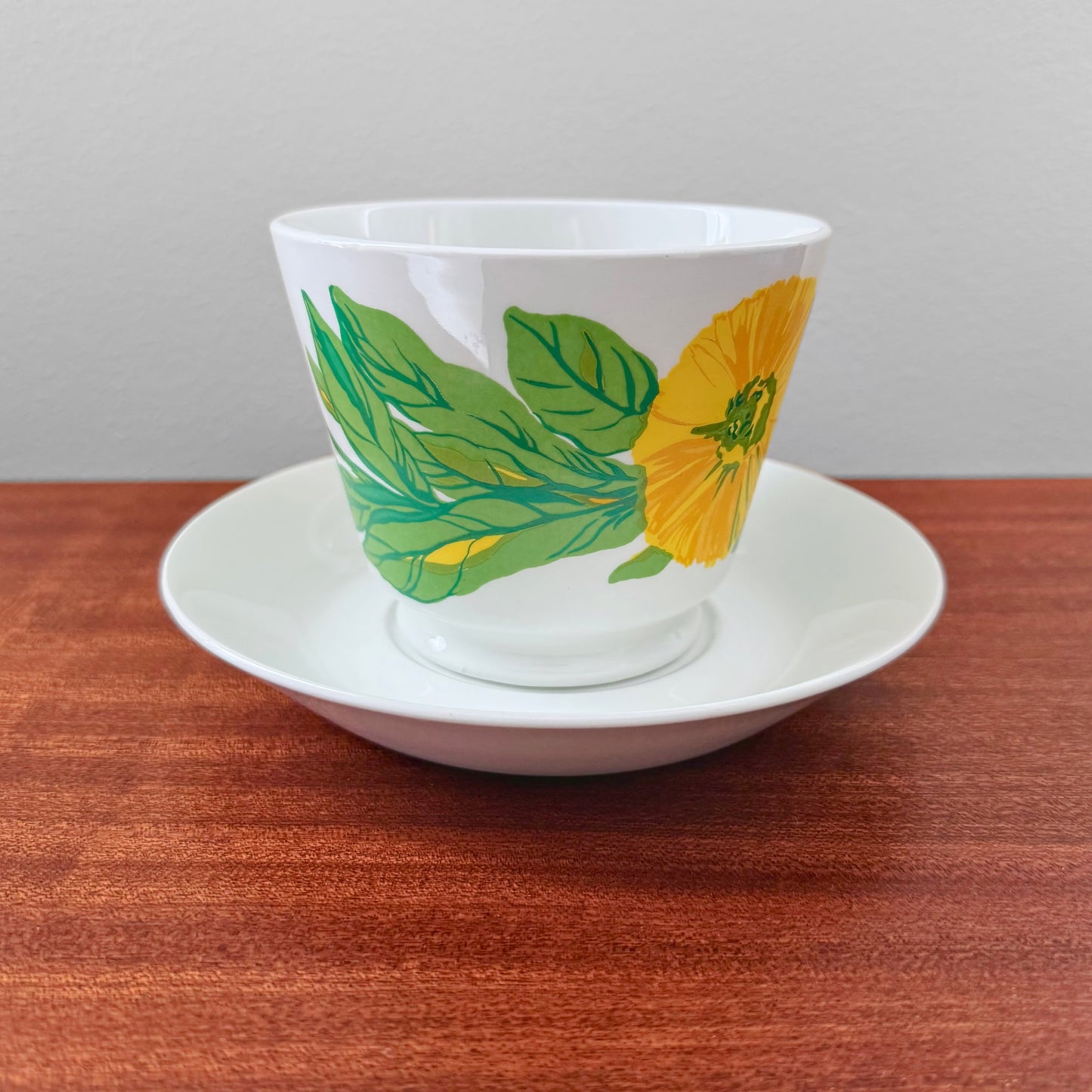 Arabia Finland Suvi Large Cocoa Cup with Saucer featuring a 1970s vintage design by Gunvor Olin-Grönqvist with vibrant green leaves and a yellow flower on white ceramic.