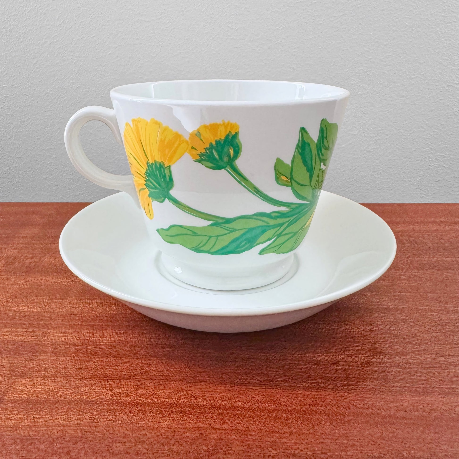 Arabia Finland Suvi Large Cocoa Cup with Saucer featuring a vintage botanical design with yellow flowers and green leaves on white ceramic, displayed on a wooden surface.