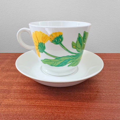 Arabia Finland Suvi Large Cocoa Cup with Saucer featuring a vintage botanical design with yellow flowers and green leaves on white ceramic, displayed on a wooden surface.