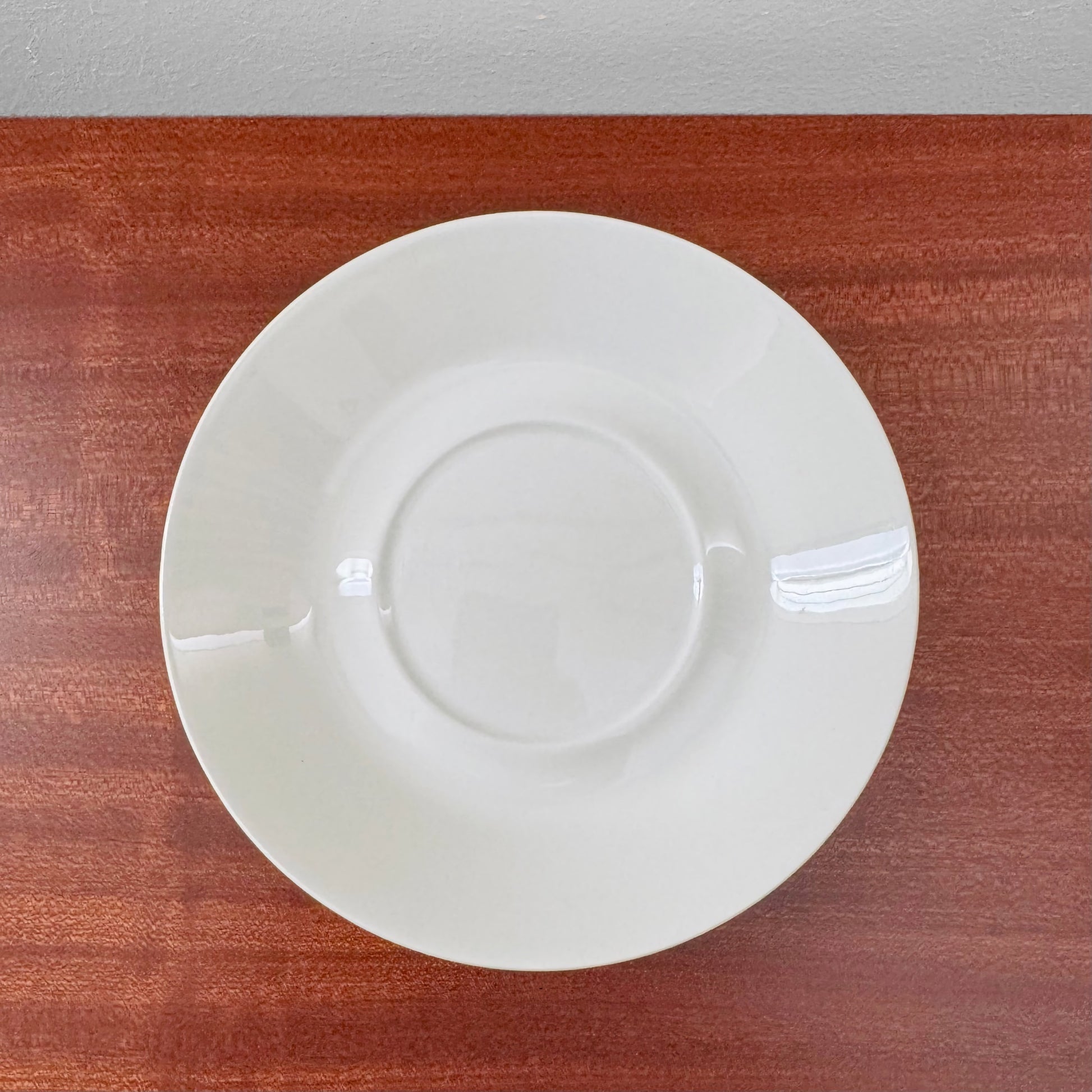 Arabia Finland Suvi Large Cocoa Cup with Saucer featuring a simple white ceramic saucer with a slight sheen, displayed on a wooden surface, part of Nordic Wares Store vintage tableware.