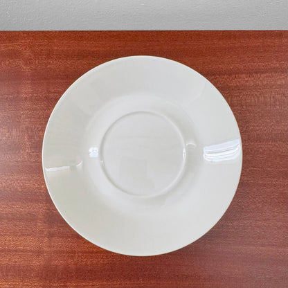 Arabia Finland Suvi Large Cocoa Cup with Saucer featuring a simple white ceramic saucer with a slight sheen, displayed on a wooden surface, part of Nordic Wares Store vintage tableware.