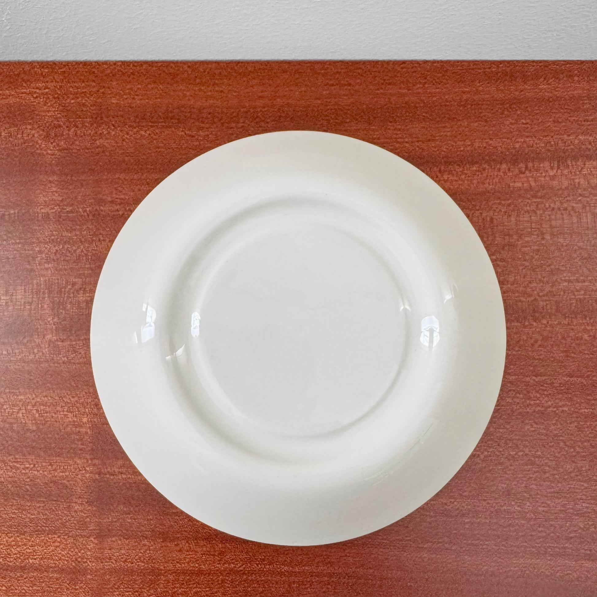 White ceramic saucer from the Arabia Finland Suvi Large Cocoa Cup with Saucer set, showing a simple, clean design with subtle signs of vintage use on a wooden surface.