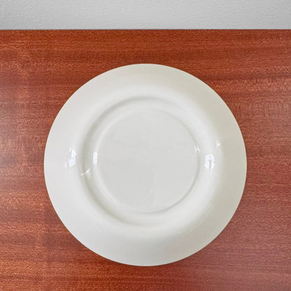 White ceramic saucer from the Arabia Finland Suvi Large Cocoa Cup with Saucer set, showing a simple, clean design with subtle signs of vintage use on a wooden surface.