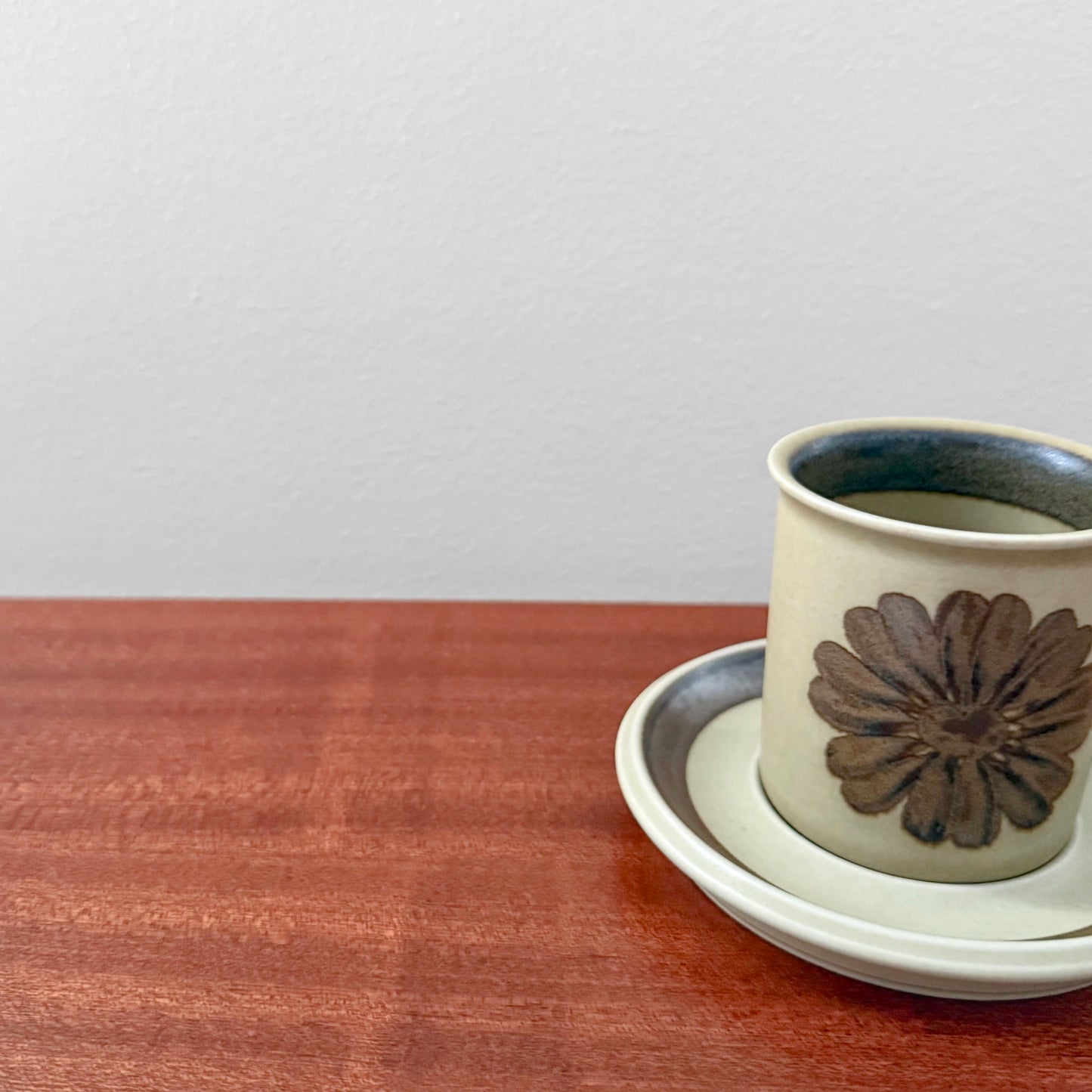 Arabia Finland Tunturi Coffee Cup with Saucer featuring vintage ceramic design with a brown floral motif, displayed on a wooden surface against a plain white wall.