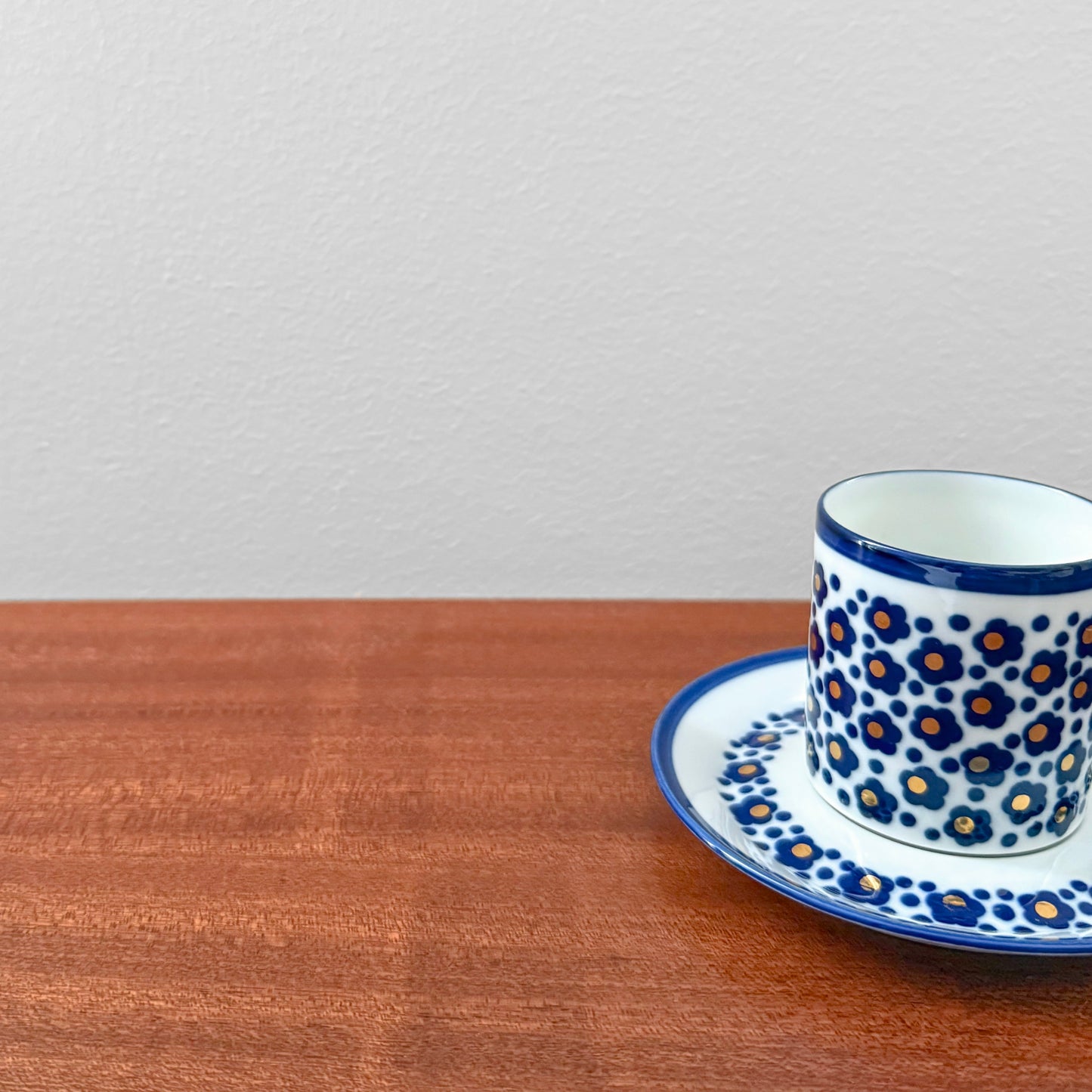 Arabia Finland Virva Espresso Cup with Saucer featuring a blue and orange floral pattern on white ceramic, displayed on a wooden surface against a light gray wall.