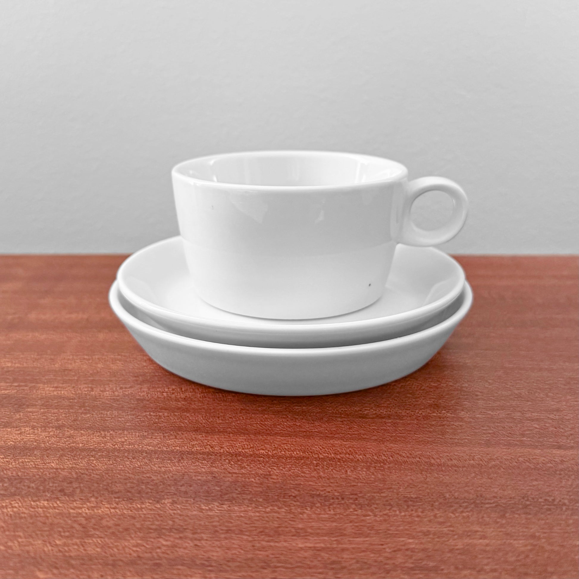 Bing & Grøndahl Hank Tea Cup Trio Set showing a white vintage tea cup with handle stacked on a saucer and a cake plate on a wooden surface, minimalist Scandinavian design.