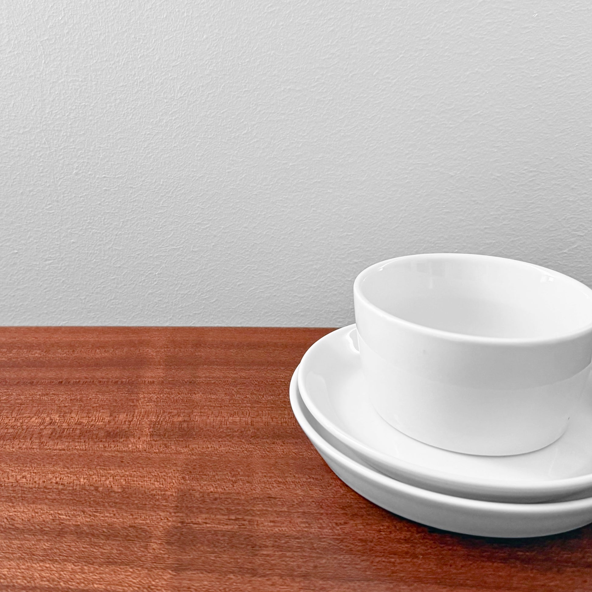 Bing & Grøndahl Hank Tea Cup Trio Set consisting of a white ceramic cup, saucer, and cake plate stacked on a wooden surface against a plain wall.