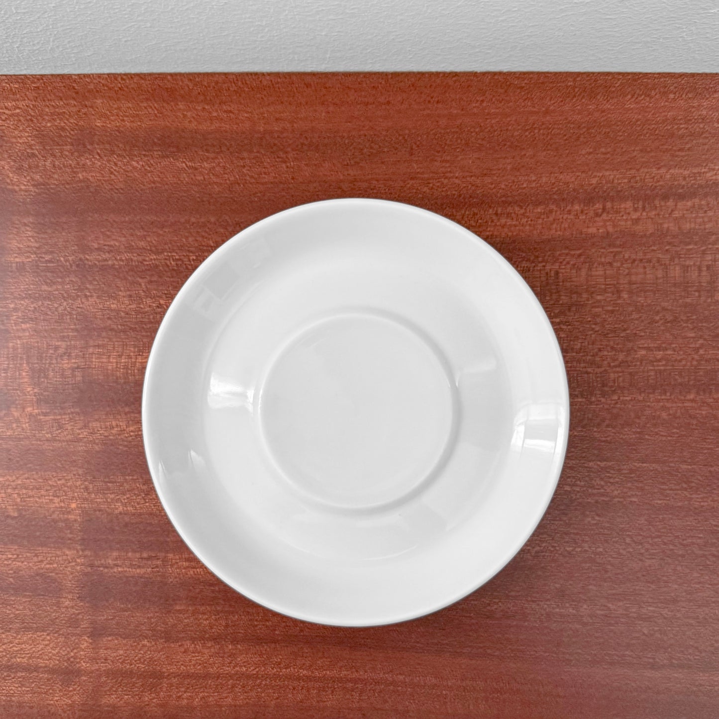 Bing & Grøndahl Hank Tea Cup Trio Set white ceramic saucer on wooden surface, showcasing minimalist Scandinavian design and craftsmanship.