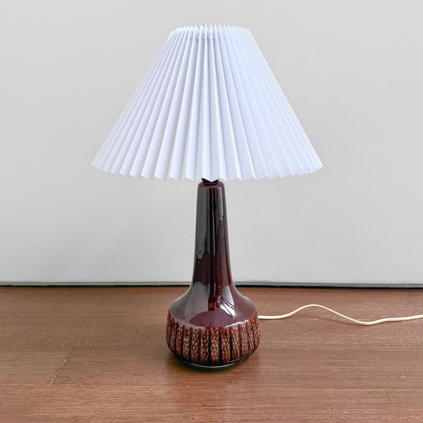 Danish Red Stoneware Table Lamp with deep red ceramic base featuring textured details and a new white plastic pleated shade, vintage Scandinavian lighting piece from the 1960s-70s.