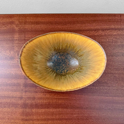 Gunnar Nylund Rörstrand ARO Stoneware Decorative Bowl in organic oval shape with brown and yellow glaze, displayed on a wooden surface, showcasing vintage Scandinavian ceramic design.