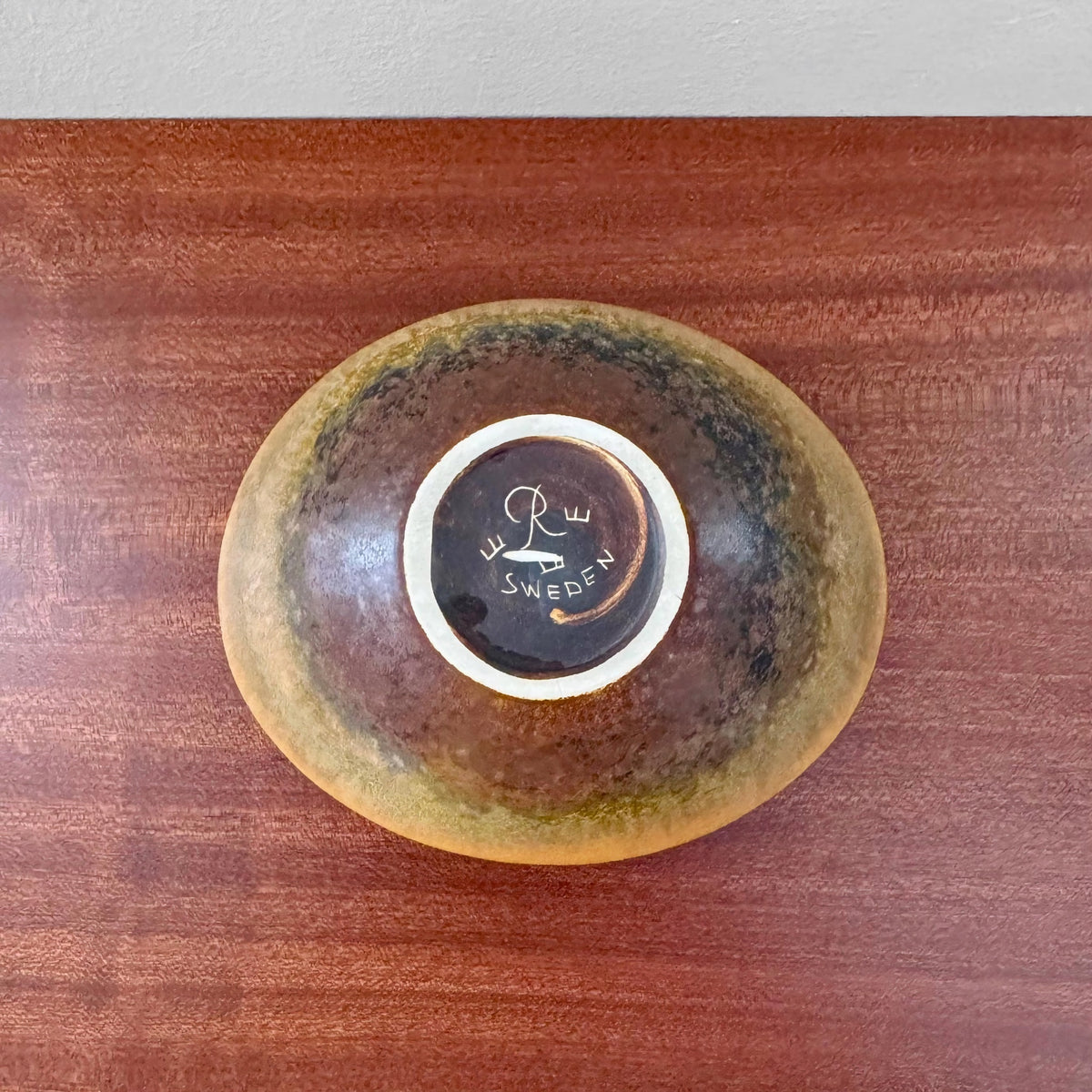 Bottom view of a Gunnar Nylund Rörstrand ARO Stoneware Decorative Bowl showing the brown glazed ceramic with the maker’s mark and Sweden stamp on a wooden surface.